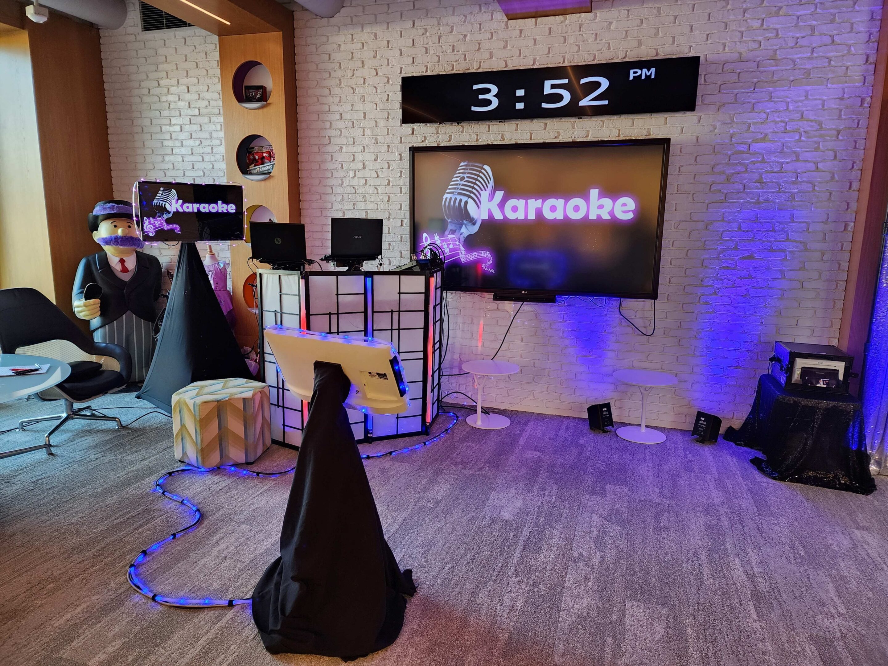 A modern karaoke dj setup in a room with a large screen displaying "Karaoke," two microphones, speakers at Hasbro Christmas Party.