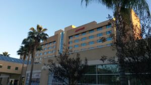 A beige multistory Marriott hotel building with palm trees in front, viewed from ground level under a clear blue sky.