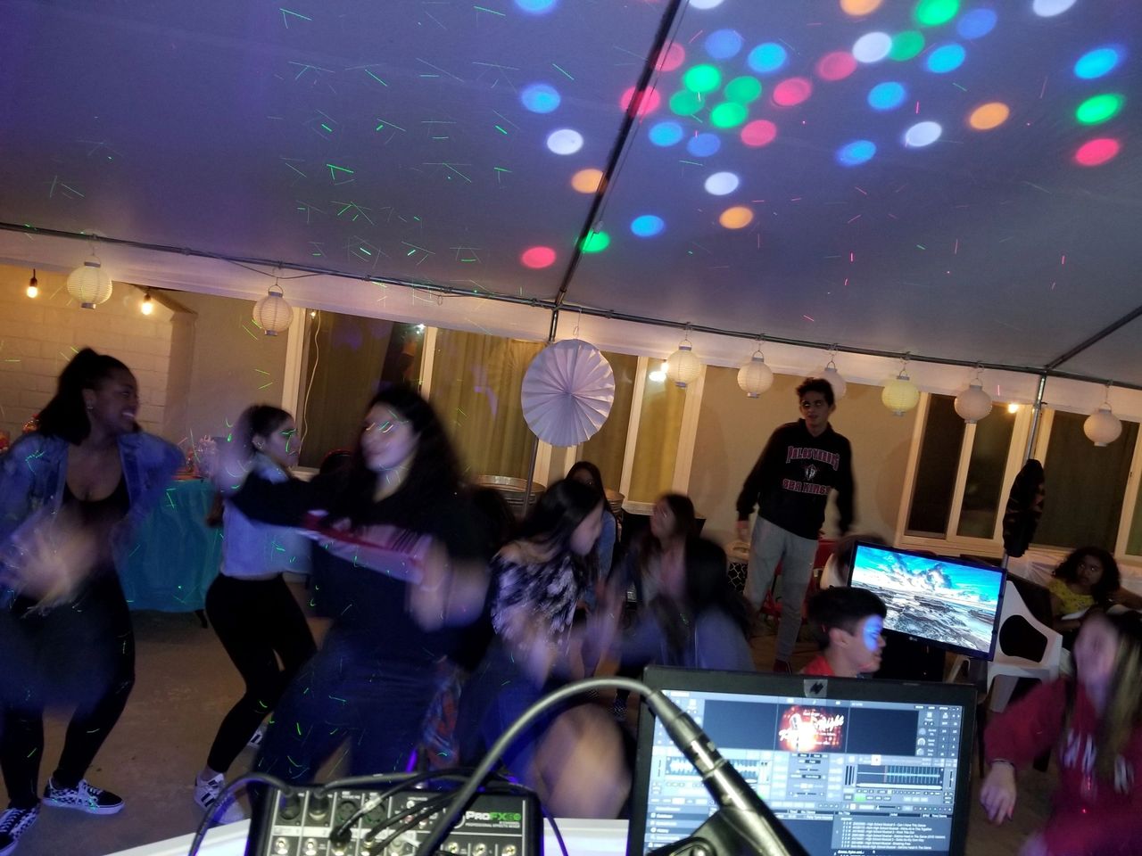 A group of kids dance under a tent with colorful lights as the kids karaoke dj plays a group dance song.