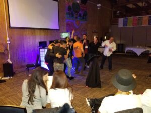 80s theme party. projector screen, some hugging and celebrating, while others sit and watch in a warmly lit room with wood-paneled walls.