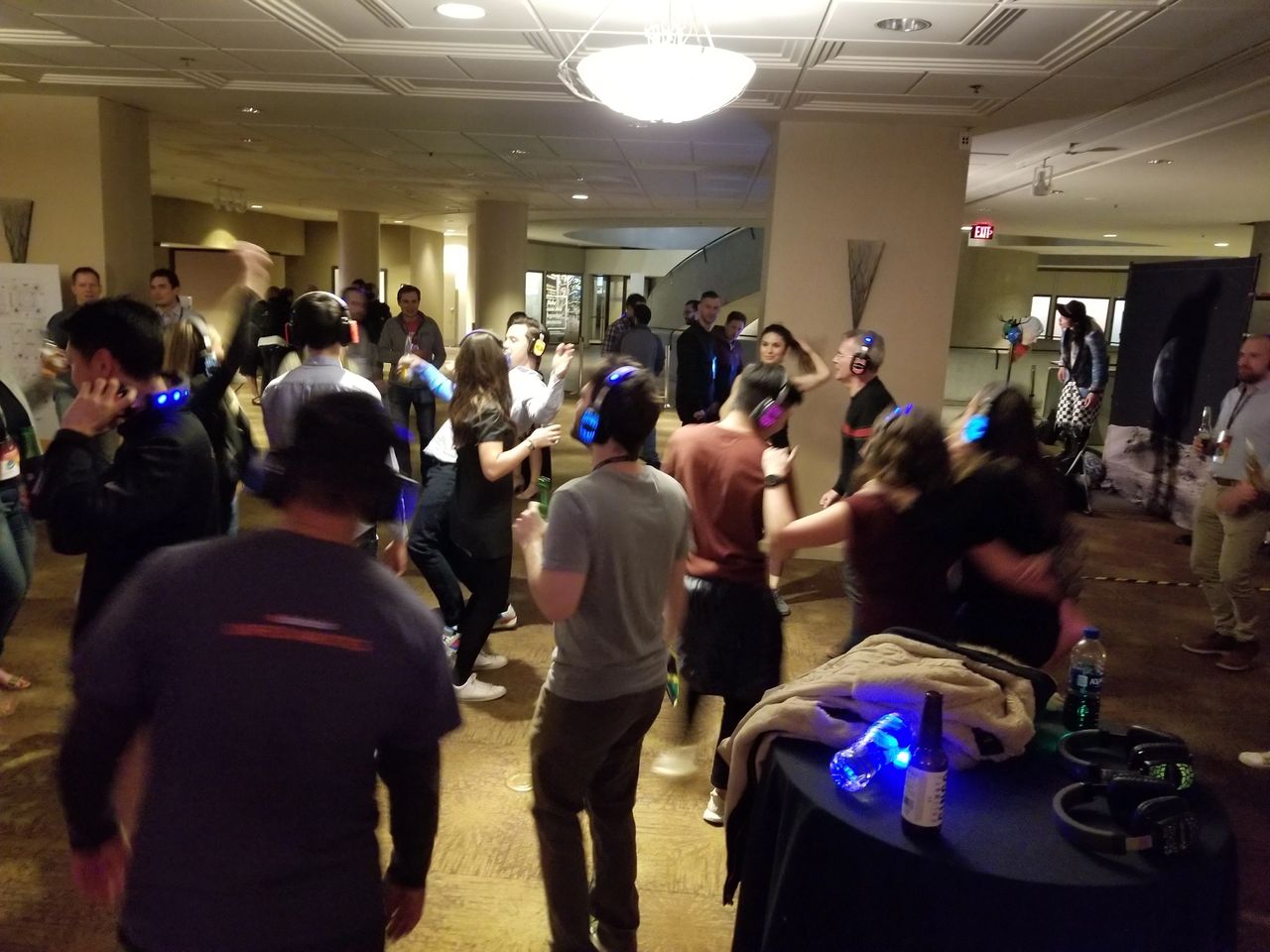 A group of people wearing headphones are dancing in a dimly lit room, likely participating in a silent disco event.