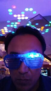 A person wearing blue LED shutter glasses under colorful disco lights with a serious expression.