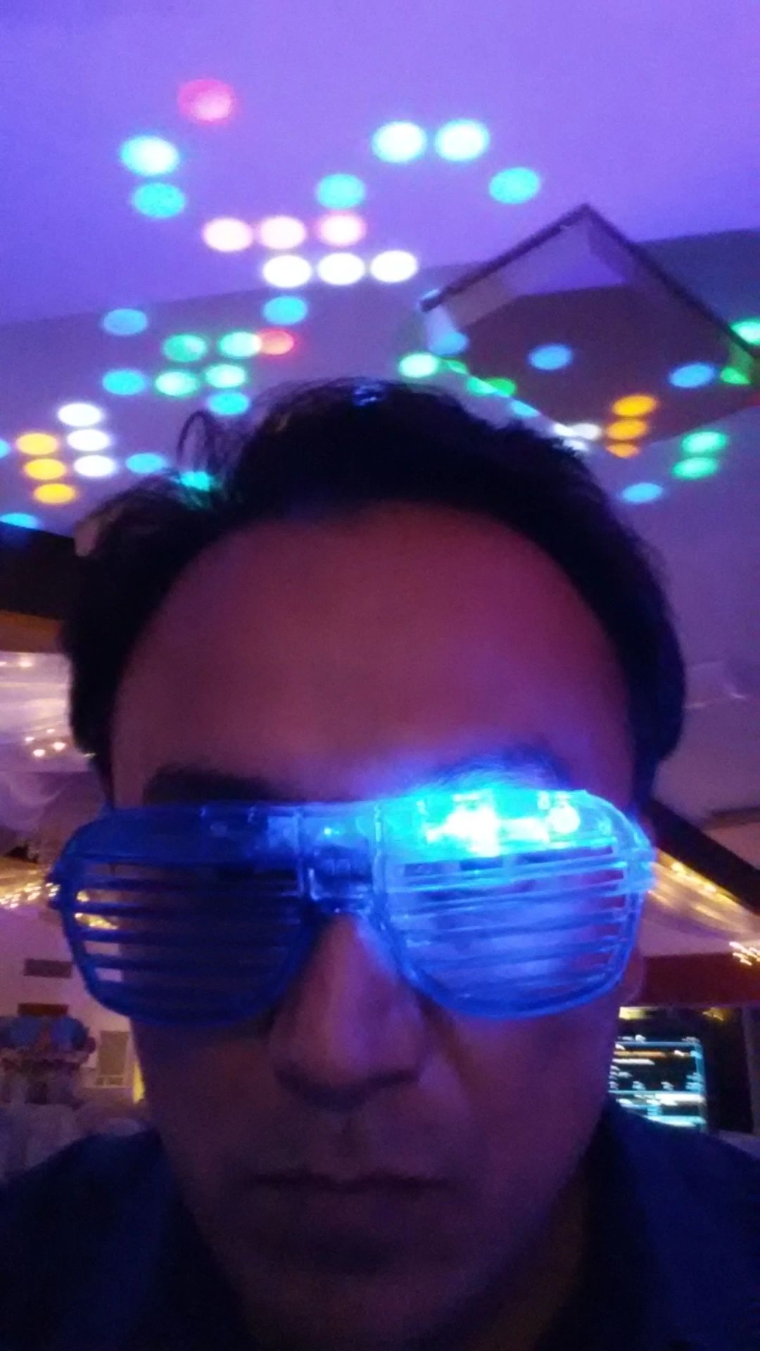 A person wearing blue LED shutter glasses under colorful disco lights with a serious expression.